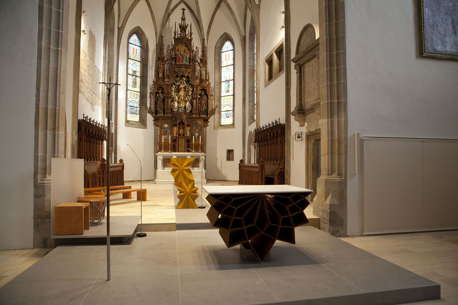Innenraum einer Kirche mit modernem geometrischem Altar und traditionellen Buntglasfenstern.